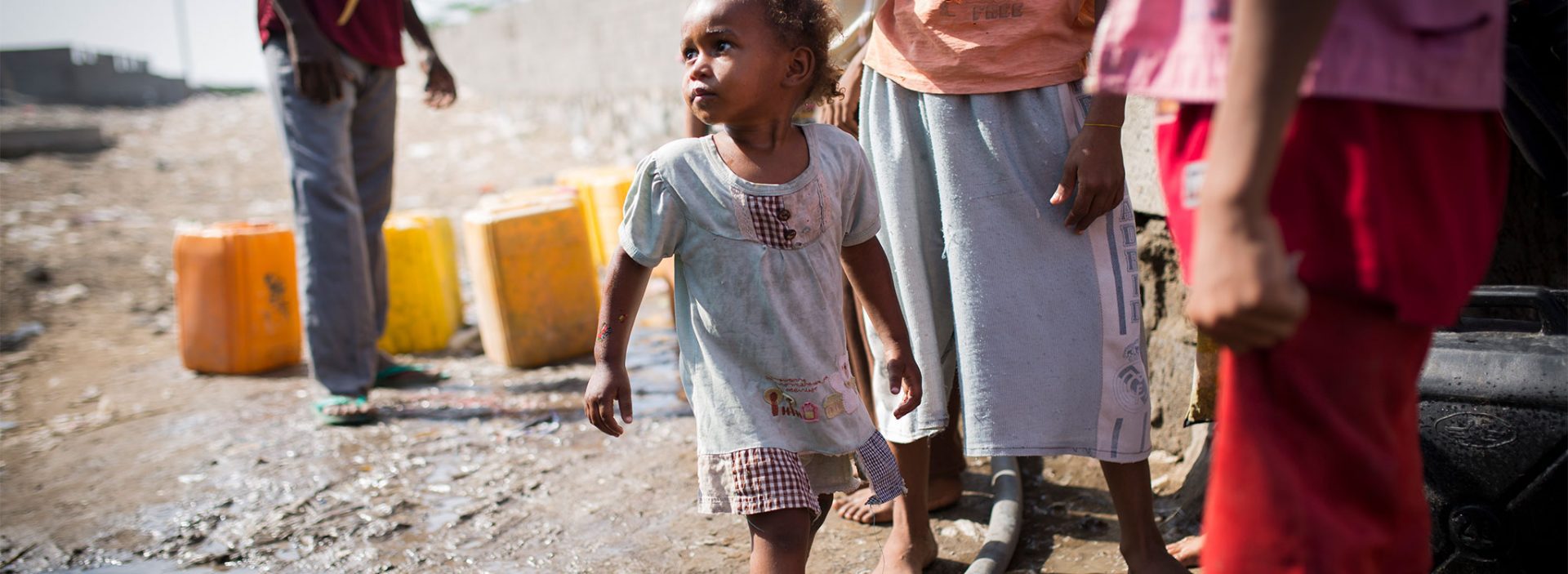 Young Yemeni girl standing with lots of water cans as her family collects water from pumps