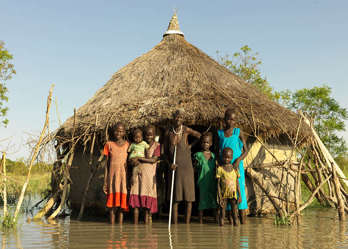 Family in South Sudan stand in front of their home which has been flooded