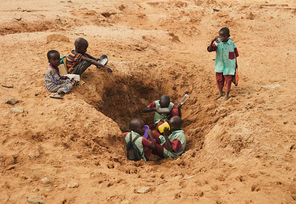 Children on their way to school in Kenya stop to drink and fill their bottles despite the water having a brown tint