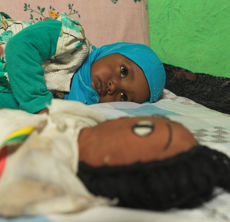 Young Munira, from Ethiopia, lying on her bed with a toy