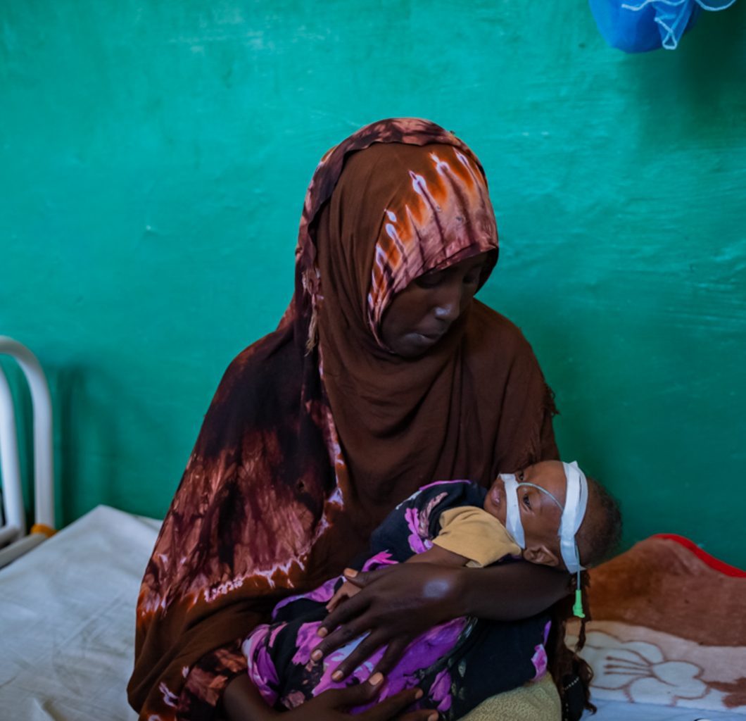 Mother sat on a bed with her undernourished child in a health clinic, Somalia