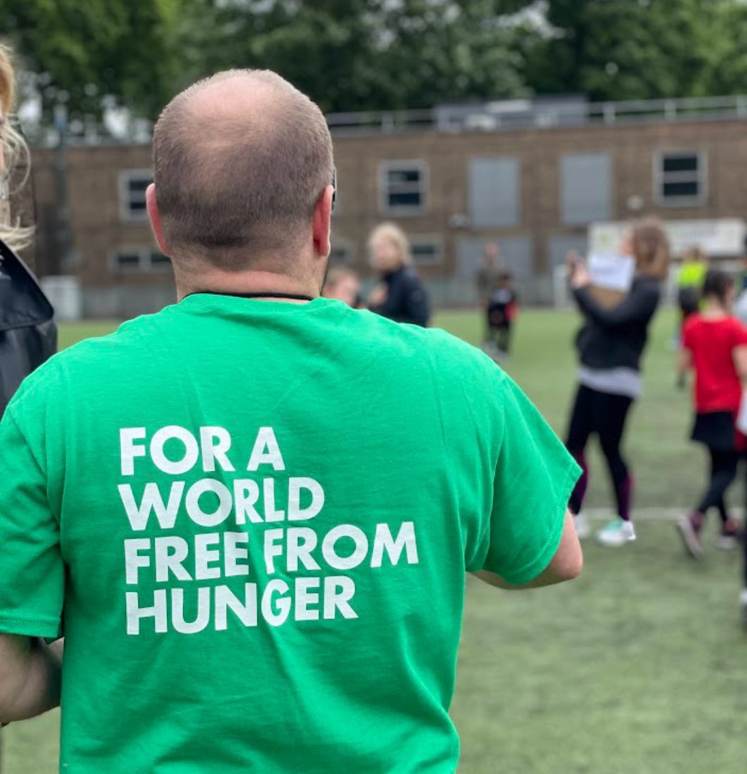 An adult, male, is stood with his back to the camera. He is wearing Action Against Hunger's t-shirt saying 'For a world free from hunger'.