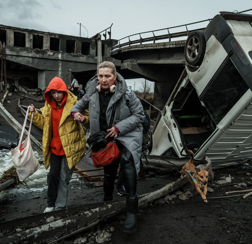Women and young teenage boy running from destroyed infrastructure including buildings and a bridge in Ukraine