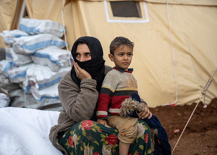 A woman sits with her son in front of a tent in Jenderes, Syria on 10 February 2023