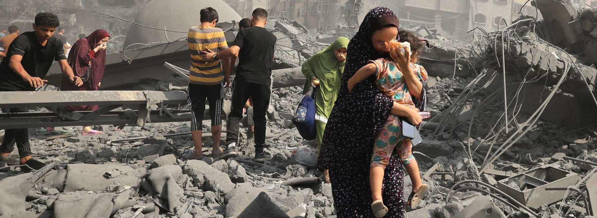 A girl carries another child in front of destroyed buildings in Gaza.
