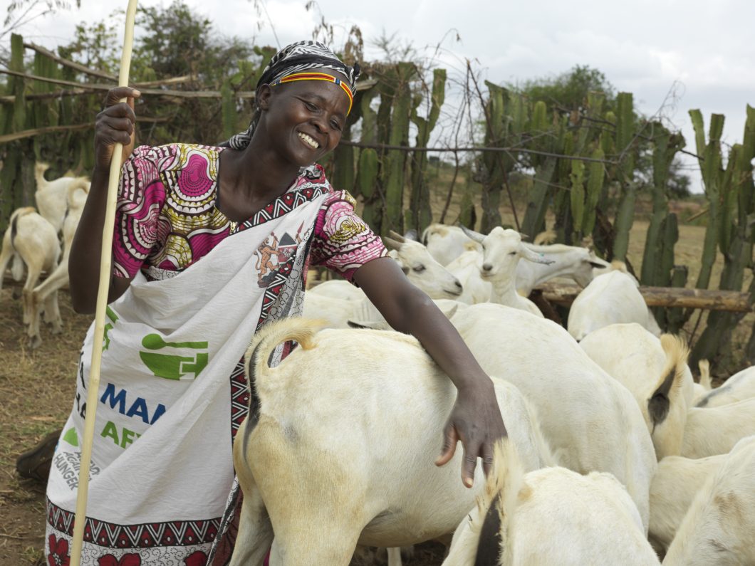 Rosalyn from Kenya, standing and smiling next to a herd of goats provided by Action Against Hunger