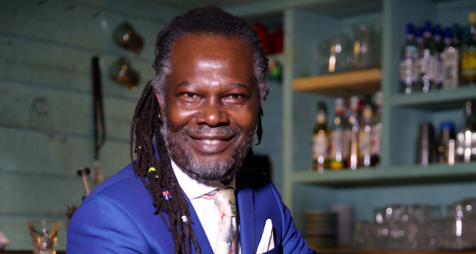 Levi Roots, chef, musician and entrepreneur, performer at Sounds of the Season festive celebration 2024, smiling at camera in green bar setting.