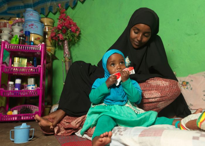 A young child eating while sitting on her mother's lap