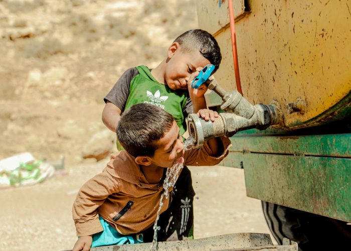 Two children drinking from a tap