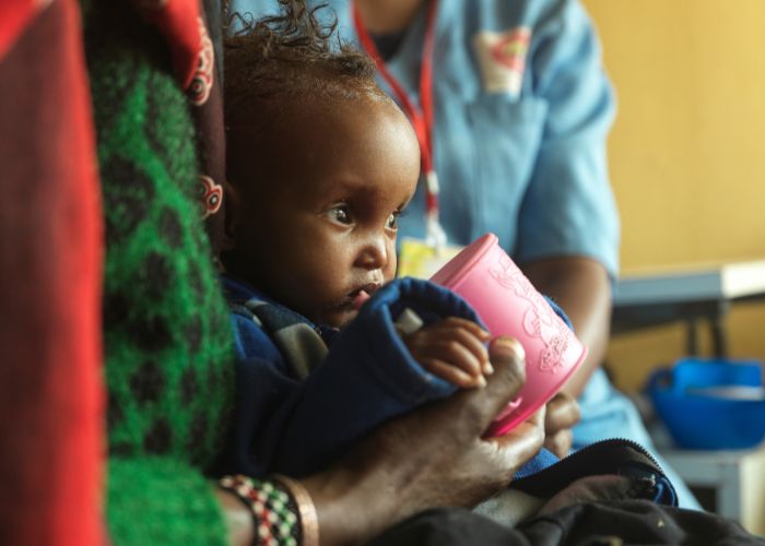A young child drinking milk sitting in their mother's lap