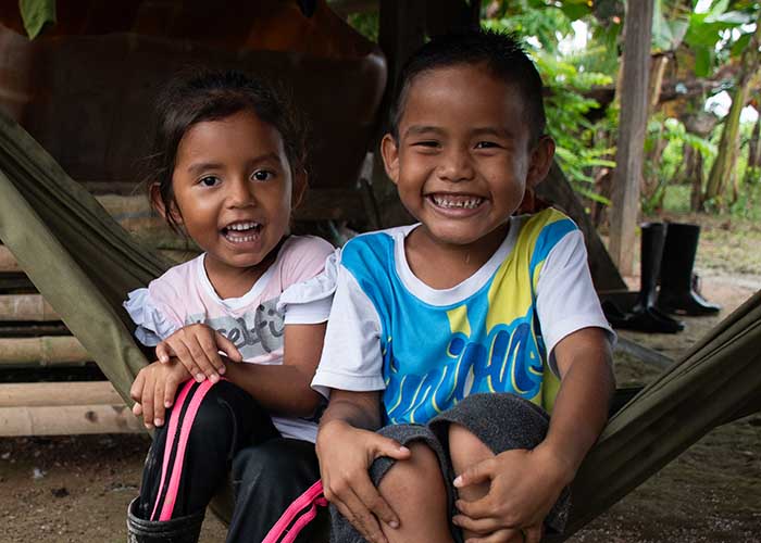 Two children from Colombia supported by Action Against Hunger. They're both sitting on a hammock and smiling.