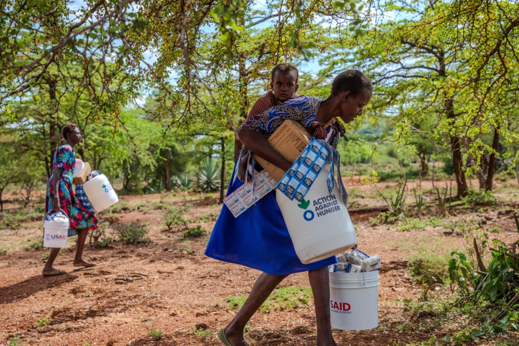 A woman carrying a child on her back holds supplies