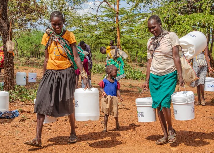 Two women carry Action Against Hunger water in Kenya.