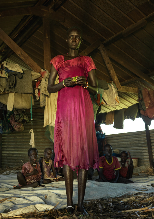 Nyamach stands with her children behind her at their home in South Sudan, which used to be a classroom before the school closed due to the flooding.